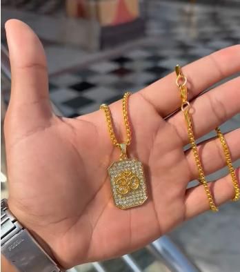 Gold necklace with a pendant held in a hand against a blurred background