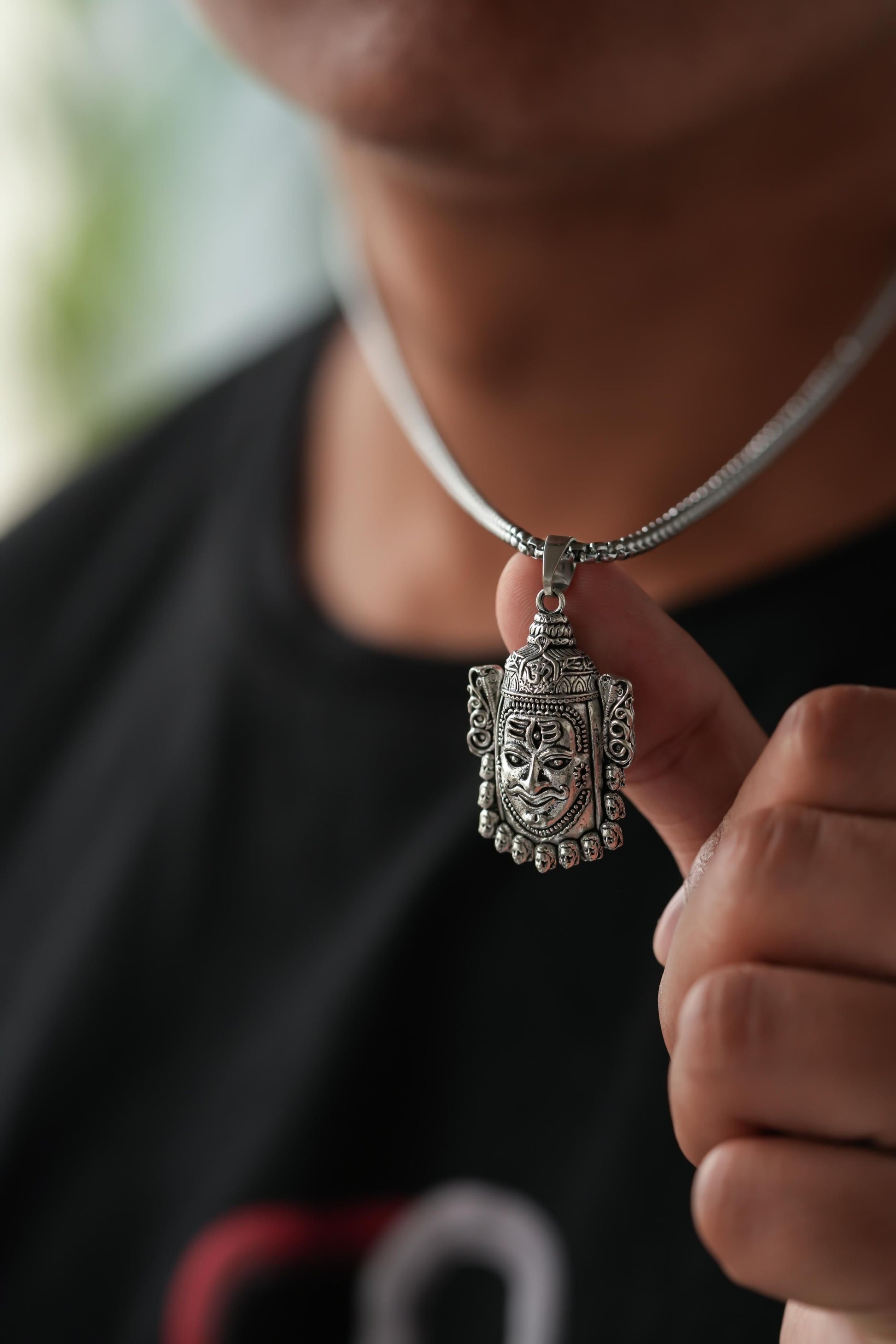 Person wearing a silver necklace with a detailed pendant