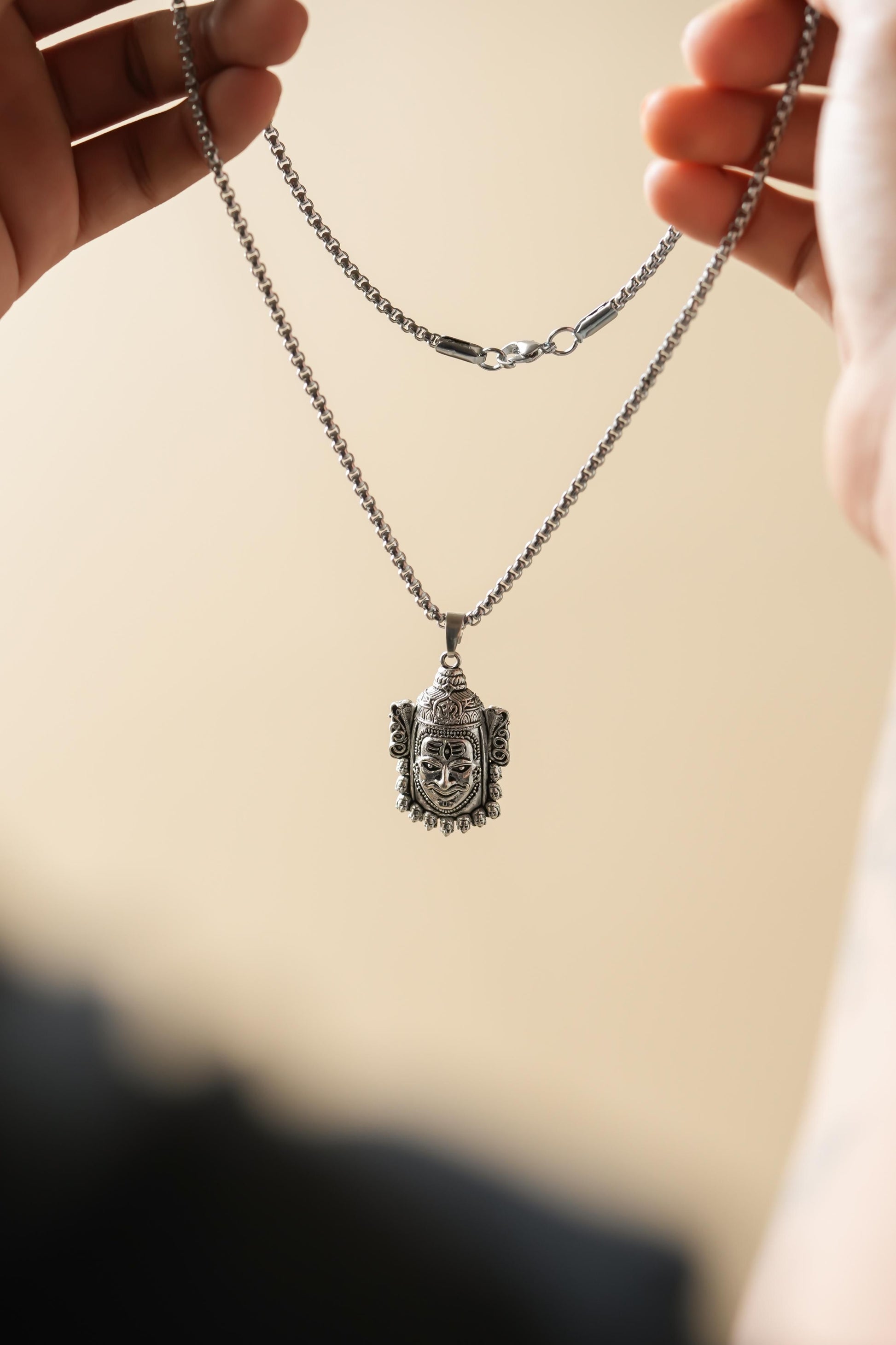 Silver necklace with a pendant held by hands against a beige background