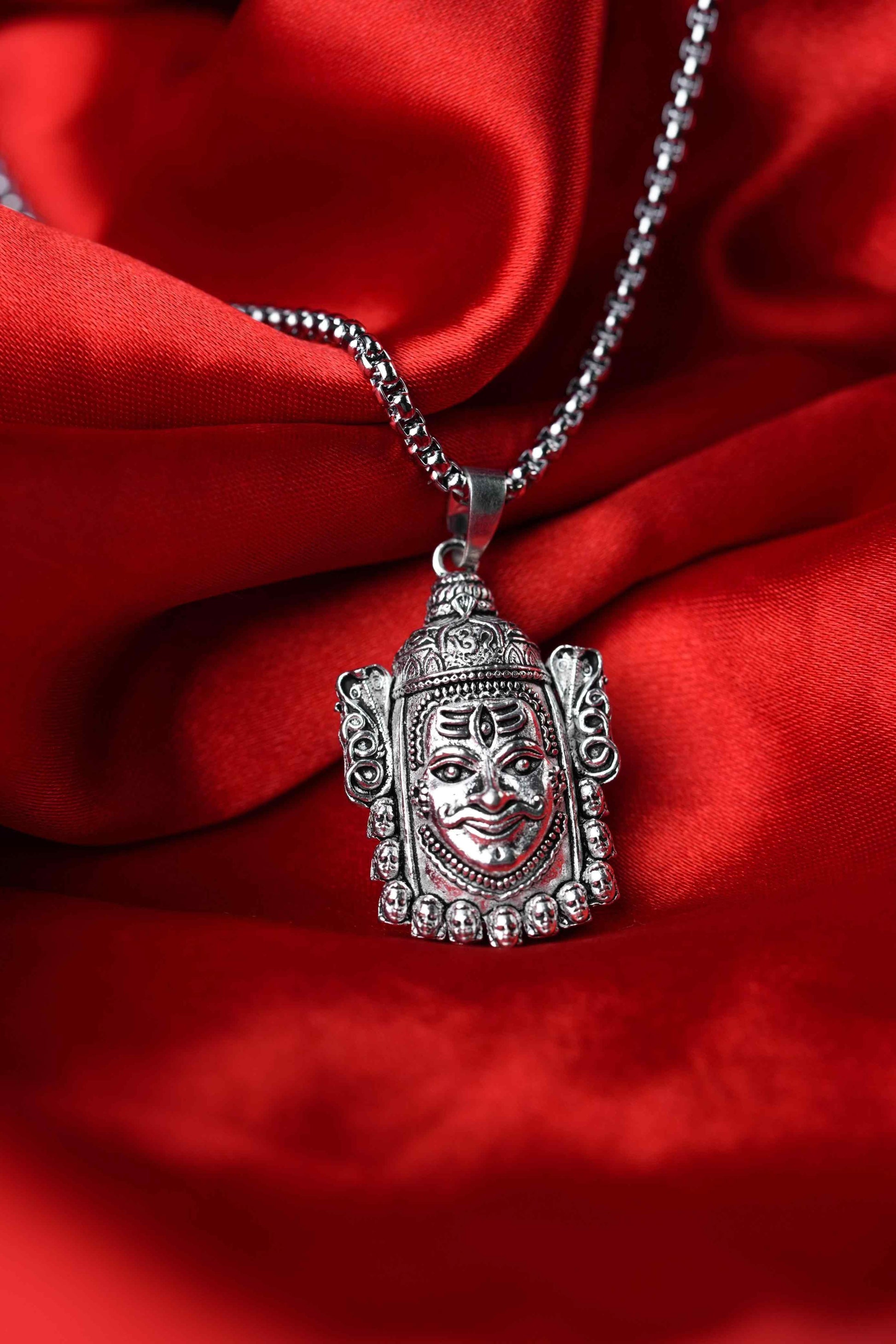 Silver pendant with face design on a red fabric background